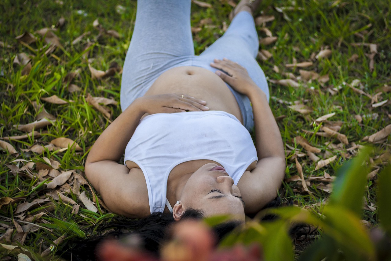 Pregnant woman laying on patch of grass.